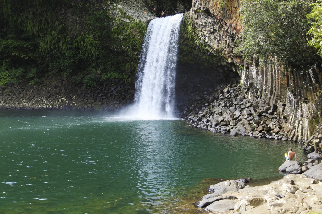 Person vor Wasserfall mit großem Badebecken 